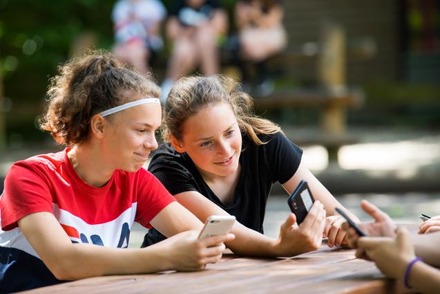 Mädchen sitzen mit Smartphone draußen am Tisch